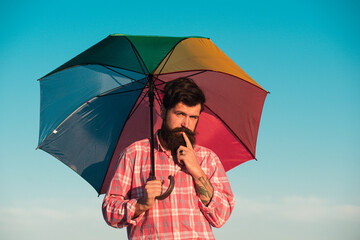 LGBT man with rainbow umbrella, long hair an beard. Gay Pride. LGBTQ concept. Isolated on sky.