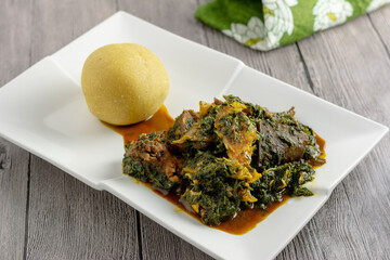 Afang soup served with eba on a white ceramic plate, wooden background