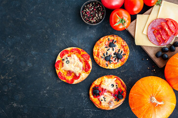 Mini pizzas for Halloween decorated with spiders and ghosts. Composition with ingredients and pumpkins on a dark background. Children's Halloween food. Place for text.