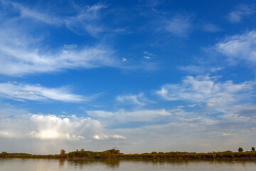 landscape on the river, blue sky with clouds, Bank edge with autumn forest