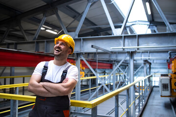 Portrait of smiling factory worker with arms crossed standing in industrial production hall.
