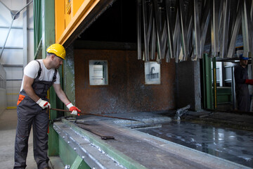 Working in metal processing factory. Metal parts being treated with zinc coating.