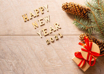 Happy new year inscription made of wooden letters on a light wooden background with a fir branch and cones. Gift boxes tied with a red ribbon in the top View. Space for text. A soft picture.