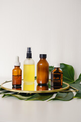 Various amber and matte glass bottles for cosmetics, natural medicine , essential oils or other liquid on a white background standing on a mirror decorated with a green monstera leaf