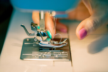 Women's fingers thread the needle of a sewing machine. Close up. Soft focus