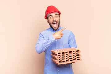 young man looking excited and surprised pointing to the side and upwards to copy space. architect...