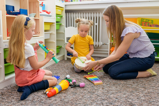 Young female therapist wearing protective face mask playing with two toddler girls during occupational child therapy.