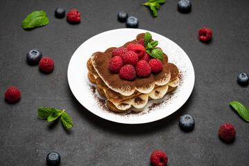 portion of Classic tiramisu dessert with raspberries and blueberries on dark concrete background