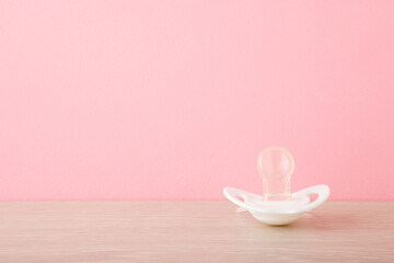 White silicone baby soother on table at pastel pink wall. Closeup. First infant toy. Empty place for text. Front view.