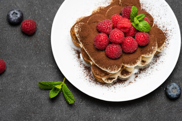 portion of Classic tiramisu dessert with raspberries and blueberries on dark concrete background