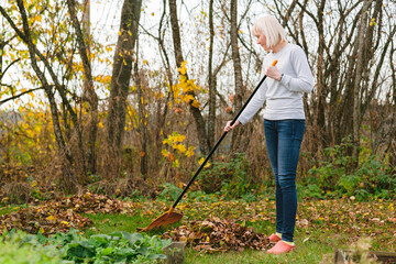 Young woman harvesting leaves. Cheerful female farmer gardener working in autumn yard.