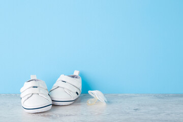 New white sport shoes and soother for infant on wooden floor at light blue wall background. Pastel color. Baby footwear. Empty place for text. Front view.