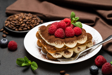 portion of Classic tiramisu dessert with raspberries and blueberries on dark concrete background