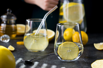 Two glasses of lemonade on a black background. Lemon slices and mint leaves float in the water and lie next to each other on the table