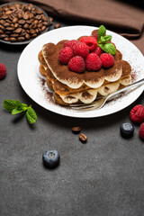 portion of Classic tiramisu dessert with raspberries and blueberries on dark concrete background