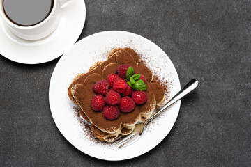 portion of Classic tiramisu dessert with raspberries and cup of coffee dark concrete background