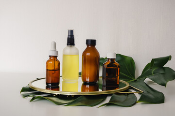 Various amber and matte glass bottles for cosmetics, natural medicine , essential oils or other liquid on a white background standing on a mirror decorated with a green monstera leaf