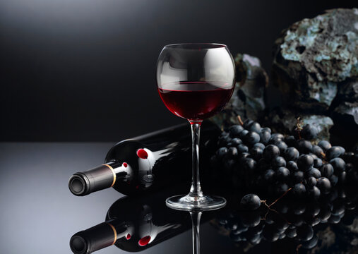 Blue grapes and red wine on a black reflective background.