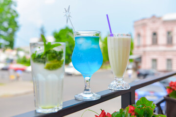 Three fresh juice drinks in tall glasses with plastic straws outside. Milkshake, blue curacao cocktail and mohito.