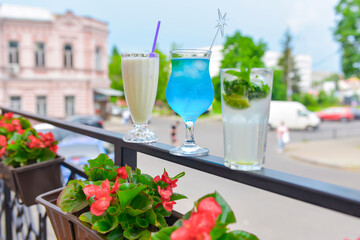 Three fresh juice drinks in tall glasses with plastic straws outside. Milkshake, blue curacao cocktail and mohito.