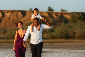 Portrait of happy multiracial family with little biracial son. Parents with toddler son walking on the beach