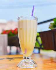 Vanilla milkshake in a tall glass with a plastic straw outside. Delicious dessert drink, refreshing summer beverage.