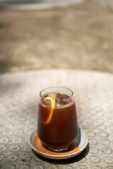 Ice black coffee and lemon in clear glass is placed on cement floor.