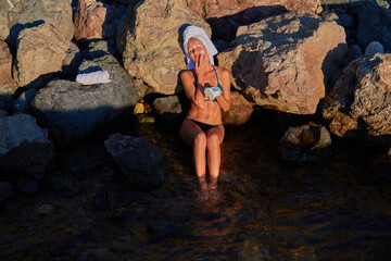 Lady applying cream on skin. Sunbathing woman sitting on rock. Relax in sea and spa. Health and meditation concept