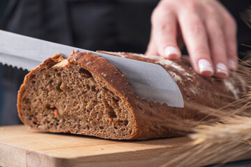 Female hands cutting  bread with a knife on the wooden board. Closeup