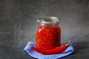 Ground hot red pepper with tomatoes in a glass jar on a dark background. A spicy seasoning made from pepper and tomatoes at home. Home cooking.