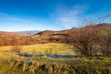 mountainous countryside in november. leafless trees on hills rolling in to the rural valley. snow capped ridge in the distance. sunny morning scenery