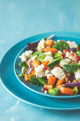 Blue plate of fresh superfoods healthy salad with red onion, tomatoes, doucette (lambs lettuce, corn salad, field salad) and feta cheese. Light blue surface
