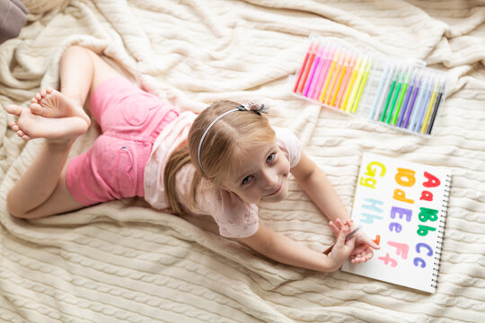 Little child learn english online at home. Homeschooling and distance education for kids. Caucasian Girl student drawing english letters at the notebook during coronavirus covid-19 quarantine