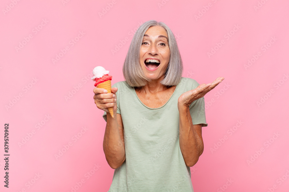 Wall mural middle age woman feeling happy, surprised and cheerful, smiling with positive attitude, realizing a solution or idea having an ice cream