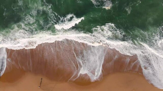 Aerial drone footage of sea waves from beach shore to horizon, brown sand and emerald water color are contrasted. Beautiful nature footage is 4K 30fps.