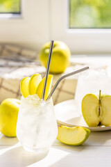 Summer cocktail with green apple and ice on the white table near window in the sunny summertime. Selective focus image with copy space
