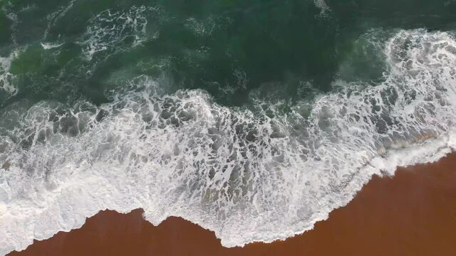 Aerial drone footage of sea waves from beach shore to horizon, brown sand and emerald water color are contrasted. Beautiful nature footage is 4K 30fps.