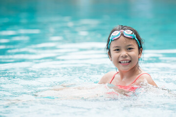 smiling child wearing swimming glasses in swimming pool. little girl playing in outdoor swimming pool on summer vacation on tropical beach island. child learning to swim in pool of luxury resort.