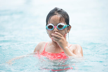 smiling child wearing swimming glasses in swimming pool. little girl playing in outdoor swimming pool on summer vacation on tropical beach island. child learning to swim in pool of luxury resort.