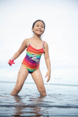 cute little girl playing in outdoor swimming pool jumping into water on summer vacation on tropical beach island. child learning to swim in outdoor pool of luxury resort. kid in colorful bathing suits