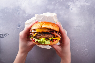 Female hands holding tasty beef burger with fried egg. Top view. Fastfood. Lifestyle