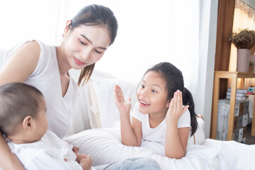 Fototapeta premium happy loving family. Love, trust and tenderness concept. Mother and child on a white bed. Parent and little kid relaxing at home. Mother and her daughters children girls playing and hugging.