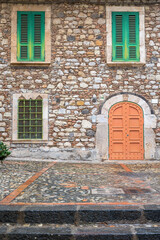 Vorderansicht eines Hauses im mediterranen Stil mit Natursteinfassade und Fensterläden