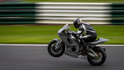 A panning shot of a racing bike on one wheel as it circuits a track.