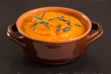 Pumpkin and carrot soup in clay bowls, earthenware with pumpkin seeds, on black slate stone table. Traditional autumn and winter dishes,warm and spicy