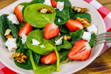 Fresh healthy salad with strawberry, spinach, walnuts and feta cheese on wooden table