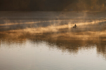 Obraz na płótnie Canvas Man fishing on a boat in a mystic foggy lake