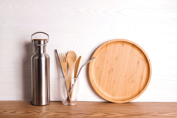 Eco set with bamboo cutlery, reusable water bottle on wooden background.