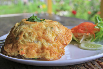 White rice topped with an omelette scented with coriander on top, served with fresh vegetables and chili sauce for added flavor.