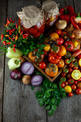 Tomatoes, peppers, onions on the table.Autumn harvest of vegetables. Glass jar with pickled tomatoes. Wooden background. Vegetable food. Still life. Tomato of different varieties. Top view.